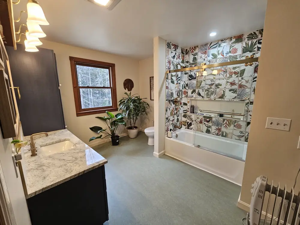 Remodeled bathroom with botanical tile tub surround, brass fixtures and navy vanity