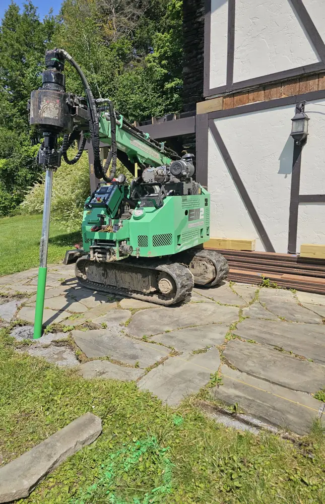 Helical pile machine setting a new steel footing beside the house