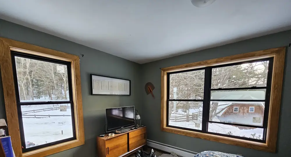 Two new black windows with stained wood casing in a green bedroom