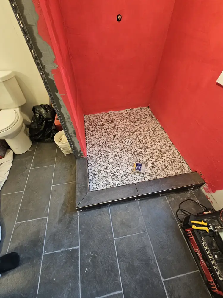 Marble hex tile floor set in the shower pan with a dark tile curb